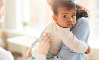 Baby being held by parent is examined by doctor.