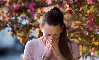 Woman sneezing in front of cherry blossom tree.