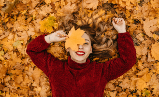Girl in sweater smiles while laying on fall leaves.