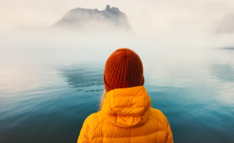 Woman in winter coat looks out onto foggy waters.